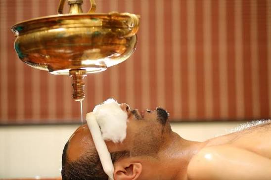Warm medicated oil being poured for Shirodhara therapy